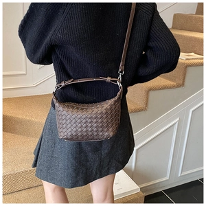Close-up of a vintage brown woven leather crossbody bag worn with a gray pleated skirt