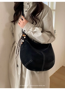 Détail du sac demi-lune noir mat avec surpiqûres blanches et pompon en perles bois