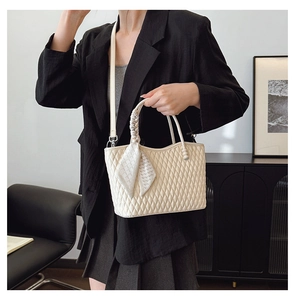Quilted beige handbag with knot handle and geometric silk scarf worn by a model