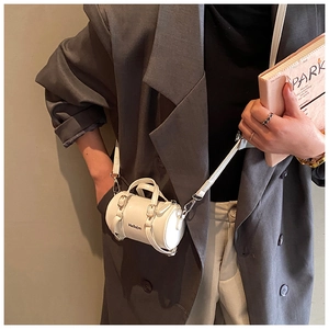 Primer plano de un mini bolso cilíndrico blanco usado con un traje gris casual