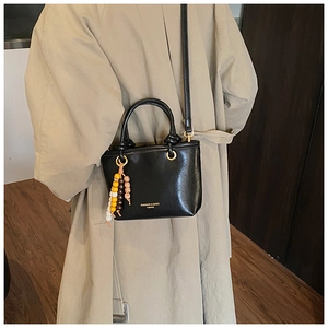 Detail of black bucket bag with gold lettering and colorful beaded charm accessory