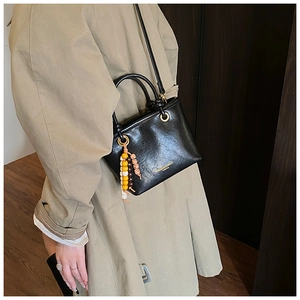 Detail of a black leather crossbody bag with a three-color wooden bead charm and gold logo