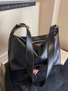 Minimalist black leather hobo bag with wide shoulder strap and gold buckle on a chair