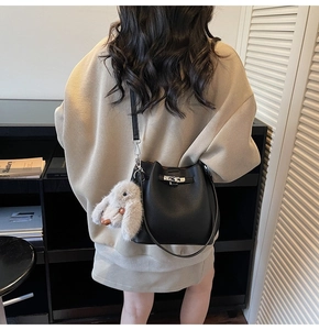 Detail of black lychee grain bucket bag with silver twist lock and plush bunny charm