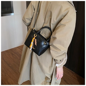 Detail of black leather bucket bag with colorful beads and crossbody strap shown on model