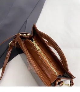 Detail of caramel brown glossy patent leather bag with gold zipper closure and layers