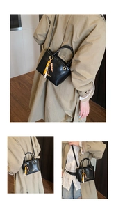 Close-up of black leather bucket bag with gold text and decorative wooden bead charm