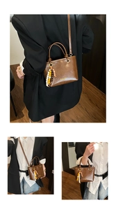 Detail of brown PU bucket bag with wooden bead charm and thin crossbody strap