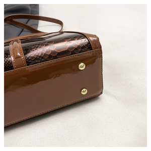 Detail of glossy brown snake-embossed faux leather handbag with golden metal protective studs