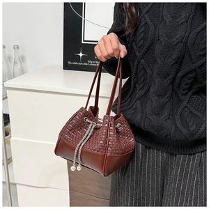 Detail of dark brown woven bucket bag featuring pearl charms and metal drawstring chains