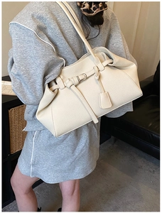 Detail of beige pebbled leather tote bag showing texture and buckle strap on model