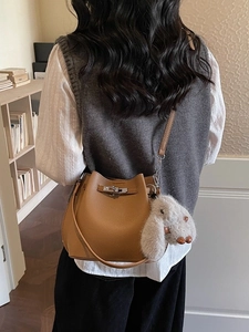 Brown litchi leather bucket bag with silver lock and plush bunny charm on shoulder strap