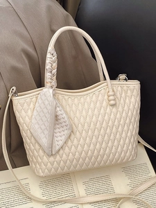 Quilted beige handbag with silk scarf handle and adjustable strap on a book