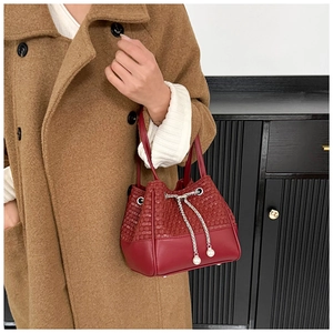 Detail of burgundy bucket bag with woven texture, metal chain and pearl drawstring