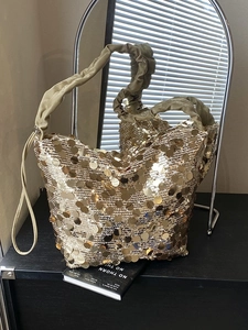 Golden sequin tote bag with ruffled handles and spacious design on a black surface