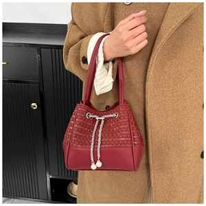 Detail of burgundy bucket bag with woven leather texture and elegant pearl drawstring accents