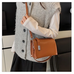 Close-up of brown litchi grain leather crossbody bag with silver twist lock and studs