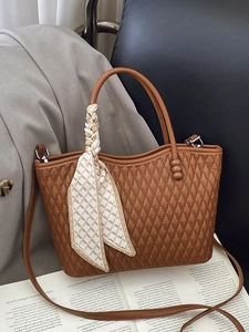 Brown quilted handbag with silk scarf handle on a grey blazer and magazine backdrop