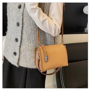 Close-up of litchi grain texture and silver metal buckle on a brown crossbody bag
