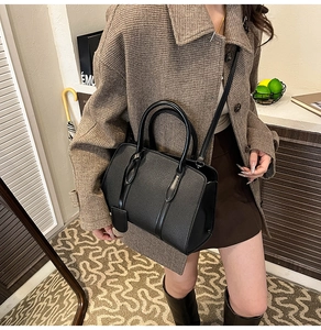 Détail d'un sac à main noir en cuir grainé avec poignées et bandoulière amovible