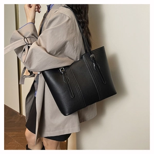 Detail of black pebbled leather tote bag with silver buckle worn with a khaki trench coat