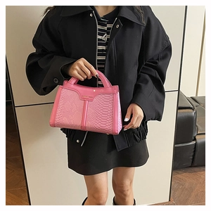 Detail of pink snake pattern handbag featuring a metal nameplate and top handle
