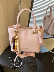 Pink minimalist crossbody bag with stylish beaded charm shown on a reflective surface