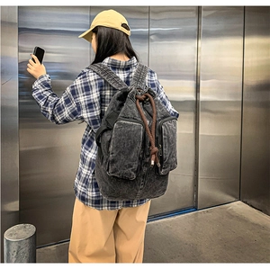 Detail of dark grey washed denim backpack featuring dual zipper pockets and drawstring