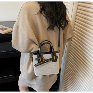Detail of grey-white fabric crossbody bag with black leather trim and gold hardware