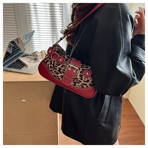 Detail of red crescent bag featuring leopard print, metal studs, and wide buckle strap