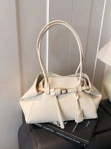 Cream litchi leather tote bag with decorative straps on a book in minimalist decor