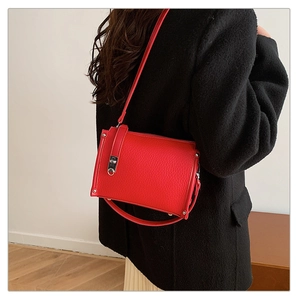 Detail shot of a red lychee pattern square bag worn by a model in a black coat