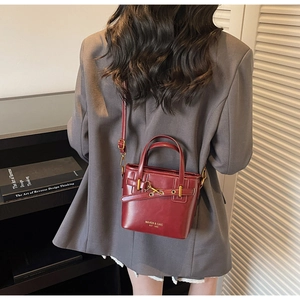 Detail view of burgundy leather bucket bag featuring gold hardware and a branded logo