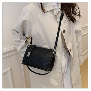 Detail of black pebbled leather crossbody bag featuring silver twist lock and metal studs
