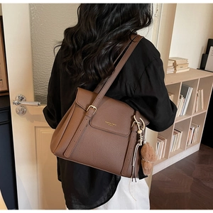 Détail du sac cabas en cuir marron à motif litchi avec boucle dorée et pompon