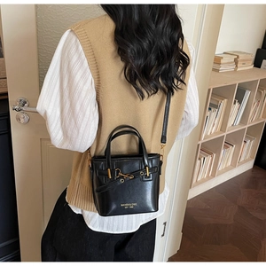 Lifestyle shot showing a black leather bucket bag with gold hardware on a shoulder