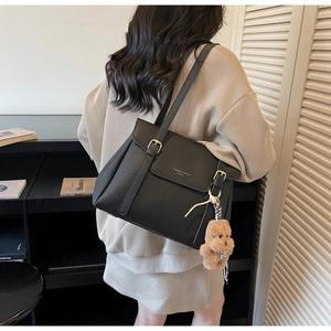 Détail du sac à bandoulière noir en texture litchi avec boucle dorée et breloque ours