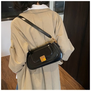 Detailansicht einer glänzenden schwarzen Baguette-Tasche mit goldener Schnalle am Trenchcoat