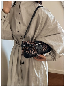 Close-up of leopard print shoulder bag with silver metal buckles on beige dress