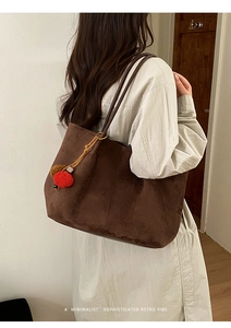 Detail view of large dark brown suede tote bag with a decorative plush pom-pom charm