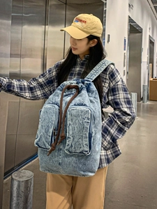Blue washed denim backpack with double front pockets and drawstring closure for daily travel
