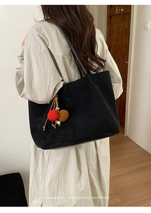 Rear view of a minimalist black large tote bag with colorful pom-pom charm on a model