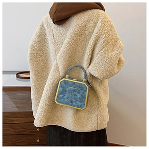 Detail of navy blue box bag with gold metal frame and twisted handle on model
