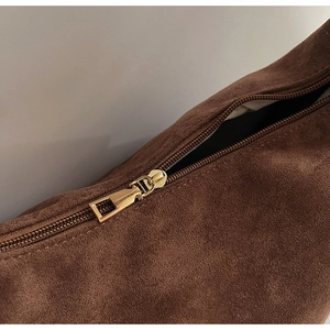 Detailed macro view of the gold-tone metal zipper on a brown suede tote bag texture