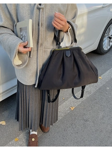 Close-up of a black pleated tote bag featuring a vintage clasp closure and round handle