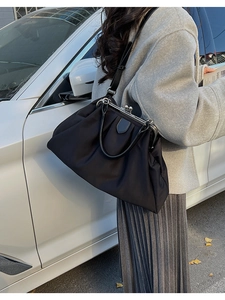 Detail of a black pleated tote bag with metal clasp and leather handle in street style