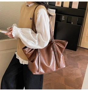 Detailansicht einer großen braunen Ledertasche mit Goldlogo und Nietendetails am Gurt