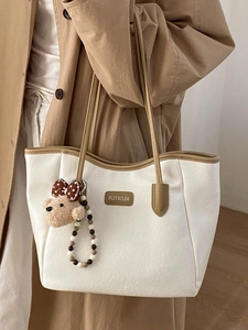 Sac cabas beige avec bordure marron et charm ours, porté sur un trench-coat élégant