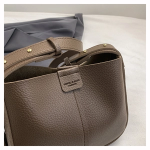 Close-up of brown litchi pattern leather bag with adjustable strap and rivet details
