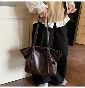 Detail der dunkelbraunen Tragetasche aus Kunstleder mit silbernen Ösen und Fashion trend Text
